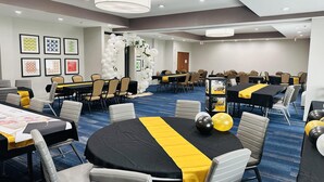 A conference room with multiple tables and chairs, decorated with balloons and tablecloths.