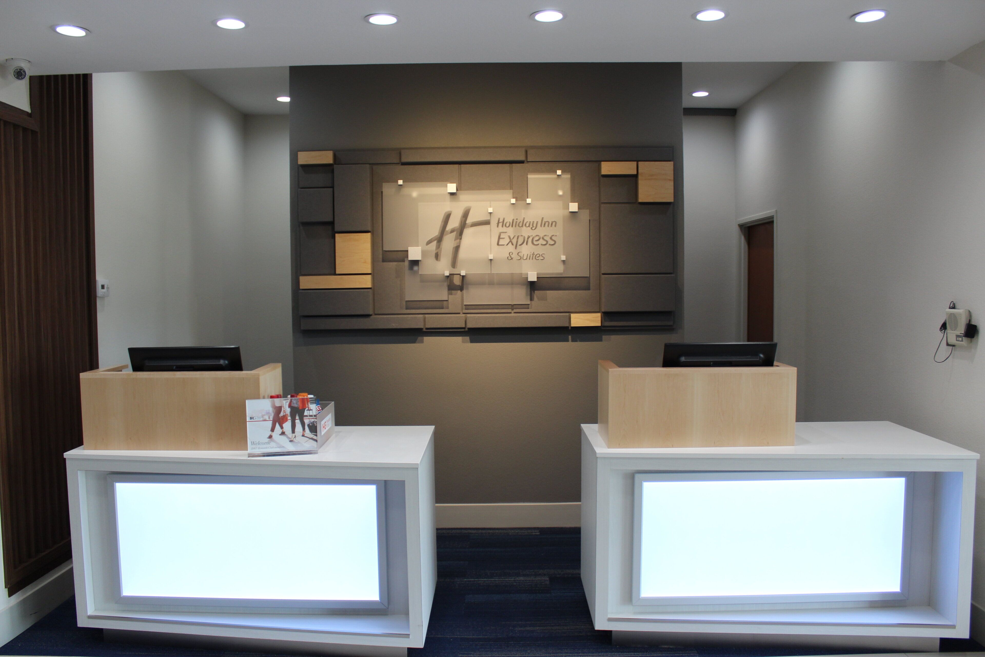 A reception area with two reception desks, a wall-mounted sign, and a ceiling with recessed lighting.