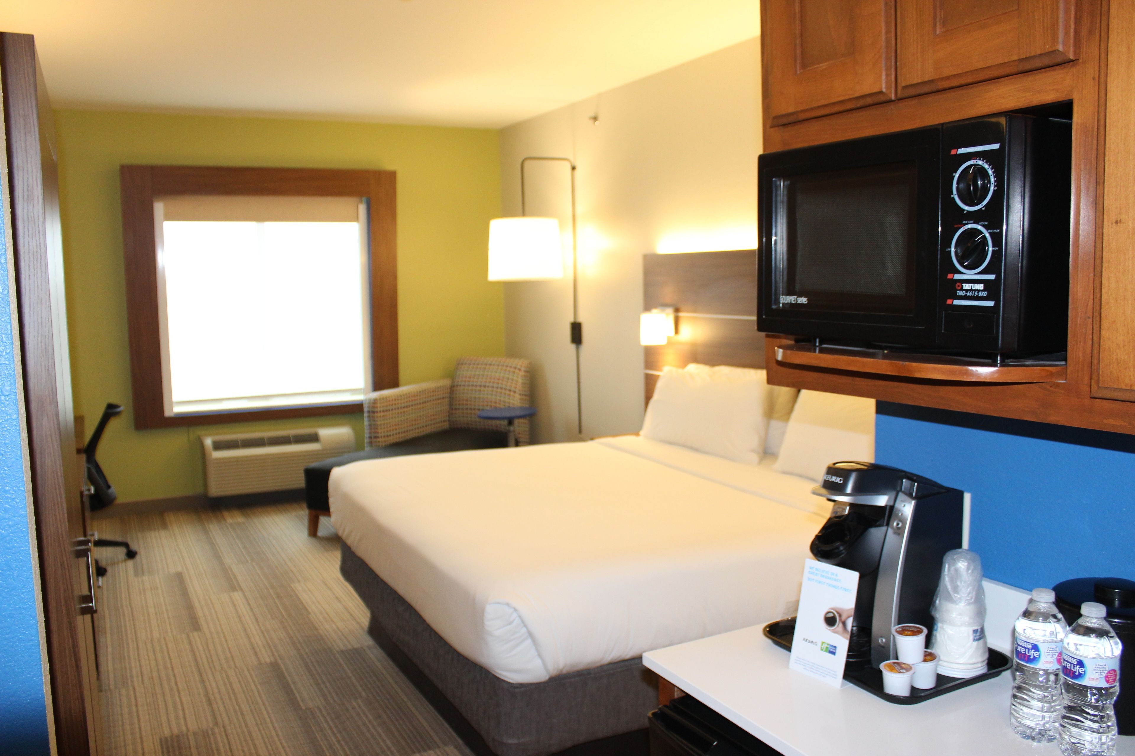 A hotel room with a bed, a microwave, a coffee maker, and bottled water.