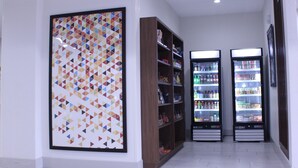 A hallway with a large geometric art piece on the left, wooden shelving units, and two refrigerated display cases with various products.