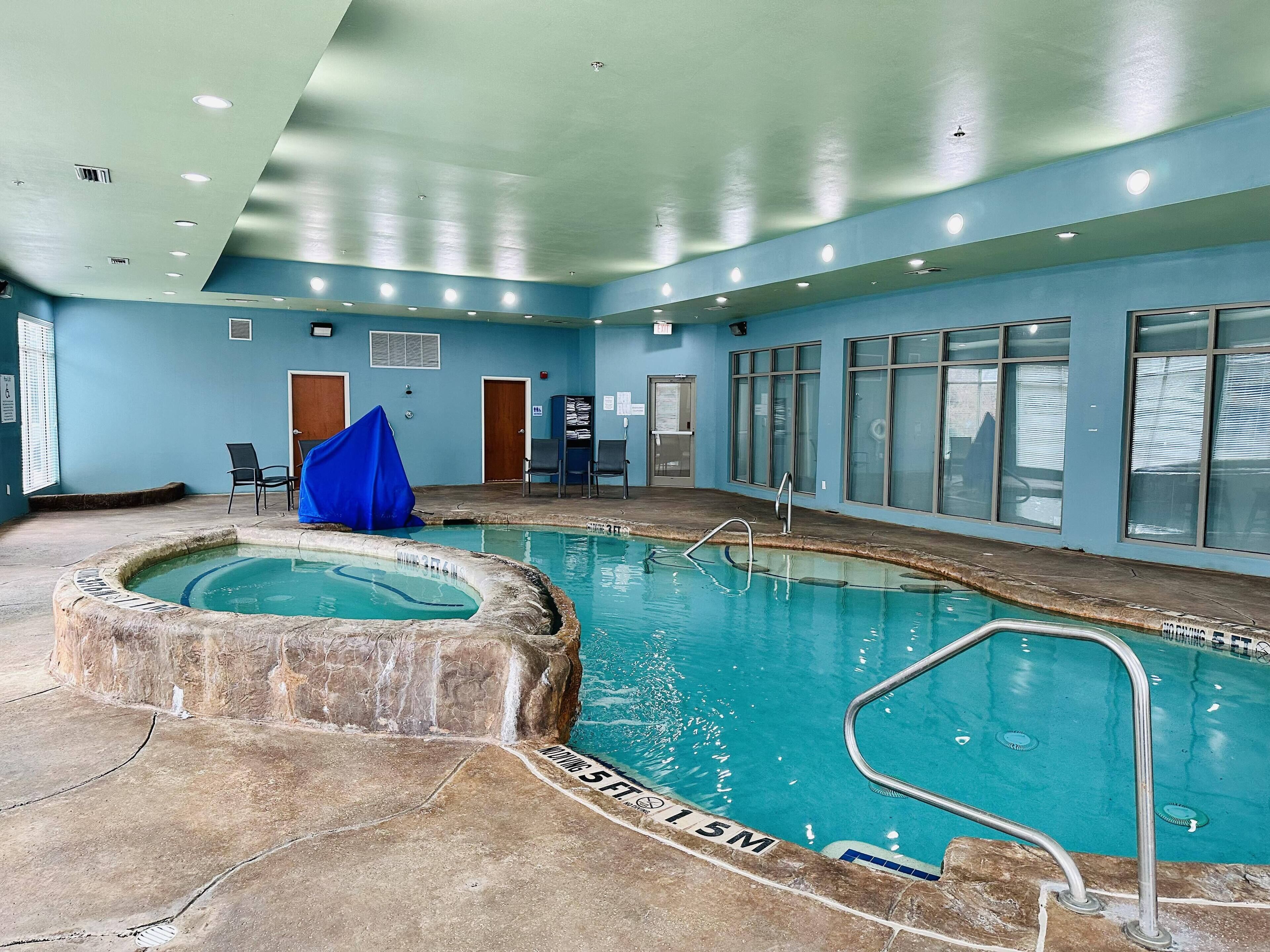An indoor swimming pool with a stone edge, a blue wall, and a ceiling with recessed lighting.