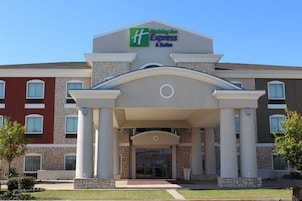 Un hotel Holiday Inn Express & Suites con fachada de piedra, una entrada central con puerta de vidrio y un cielo azul despejado.