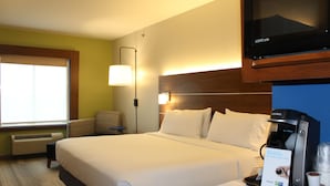 A hotel room with a large bed, a television, a coffee maker, and a sign indicating the coffee maker is available 24 hours.