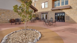 A courtyard with outdoor seating, a small tree, and a stone wall. - Drury Inn & Suites Las Cruces (Las Cruces)
