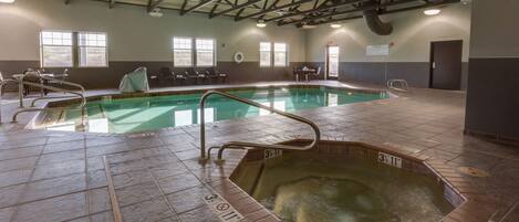An indoor swimming pool with a hot tub, tiled flooring, and a high ceiling with beams.
