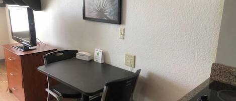 A small kitchenette with a stove, a microwave, and a coffee maker. There is a dining table with two chairs and a framed picture on the wall.