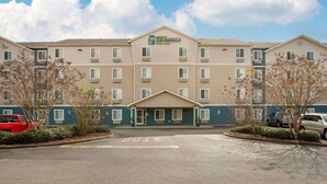 A multi-story hotel with a central entrance, parking lot, and a clear sky.