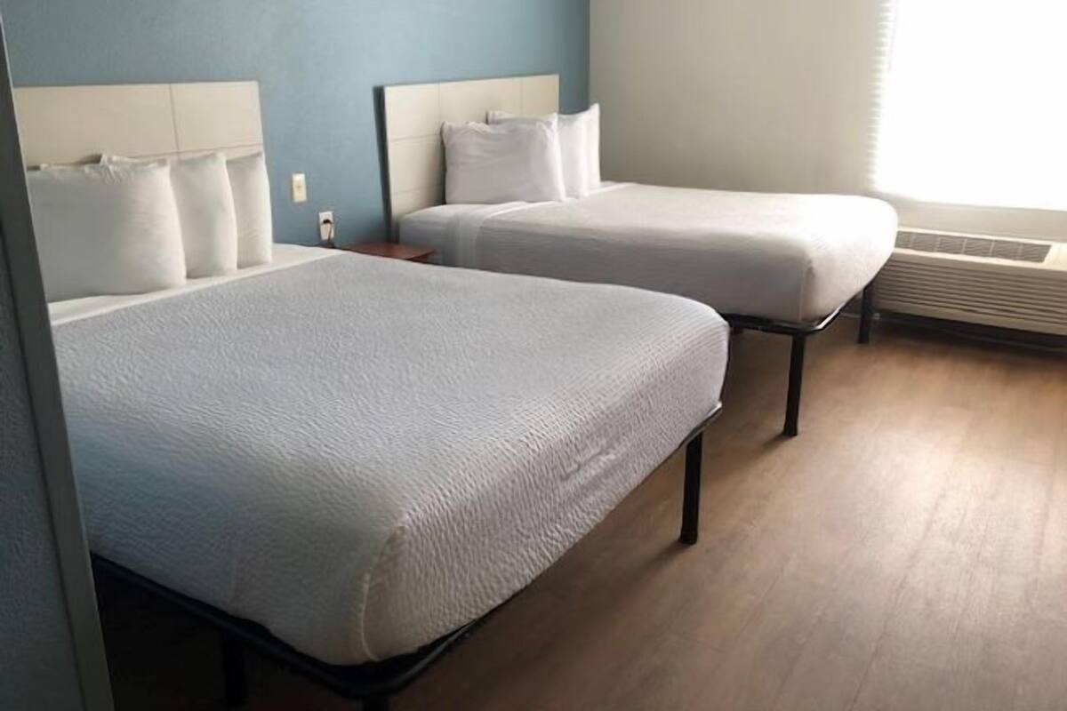 Habitación de hotel con dos camas individuales, una mesita de noche y una ventana con persianas.