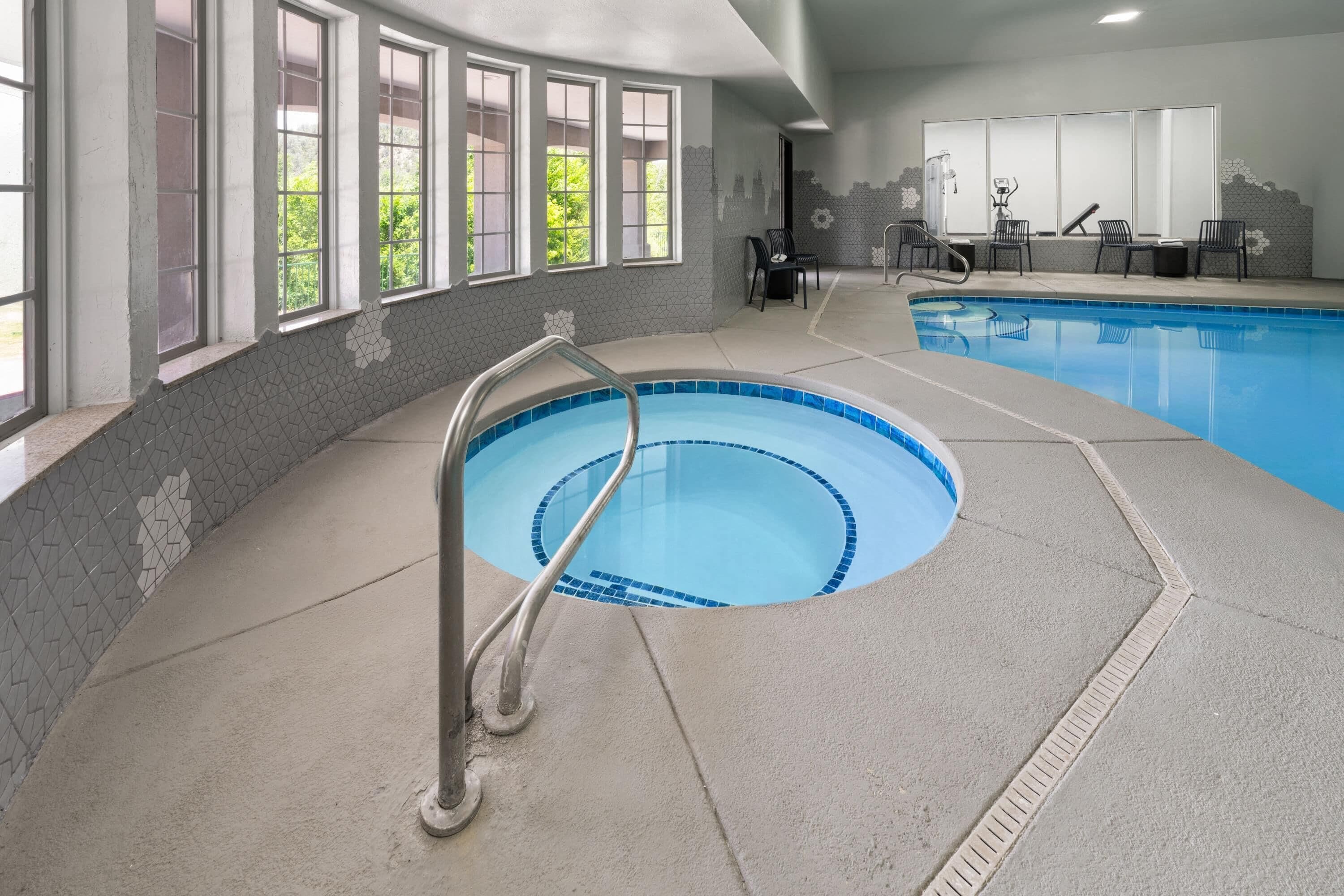 An indoor swimming pool with a clear view of the surrounding area, including windows and a seating area.