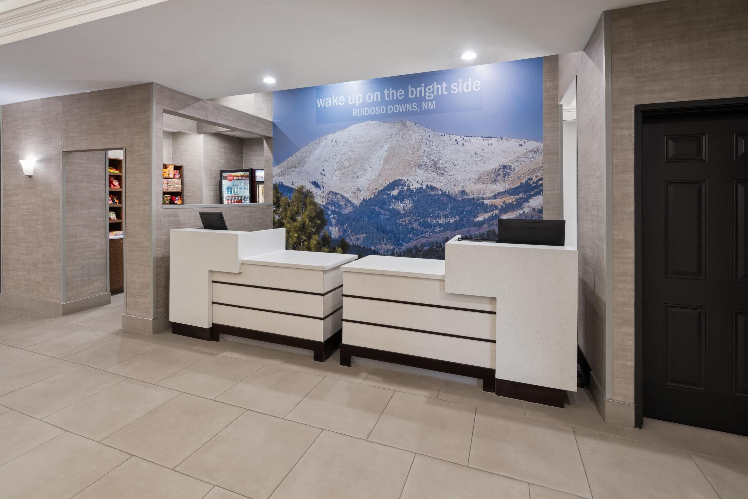 A reception desk with a poster of a mountain landscape, a refrigerator, and a vending machine.