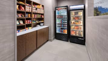 Een plek met snacks en drankjes, met planken vol chips, ontbijtgranen en andere lekkernijen, en twee drankautomaten.