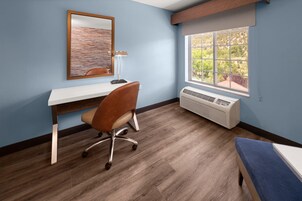 A room with a desk, chair, air conditioning unit, and a window with a view.