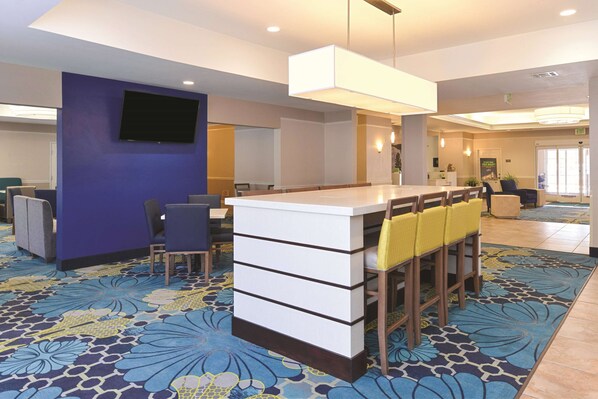 A hotel lobby with a reception desk, seating area, and a large screen. - La Quinta Inn & Suites by Wyndham Ruidoso Downs (Ruidoso Downs)