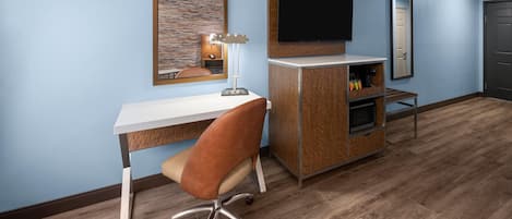 Une chambre d’hôtel équipée d’un bureau en bois, d’une chaise, d’un téléviseur à écran plat, d’un minibar et d’un miroir.