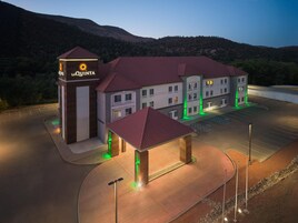 Un hotel con un letrero llamativo, varios edificios, un estacionamiento y montañas al fondo.