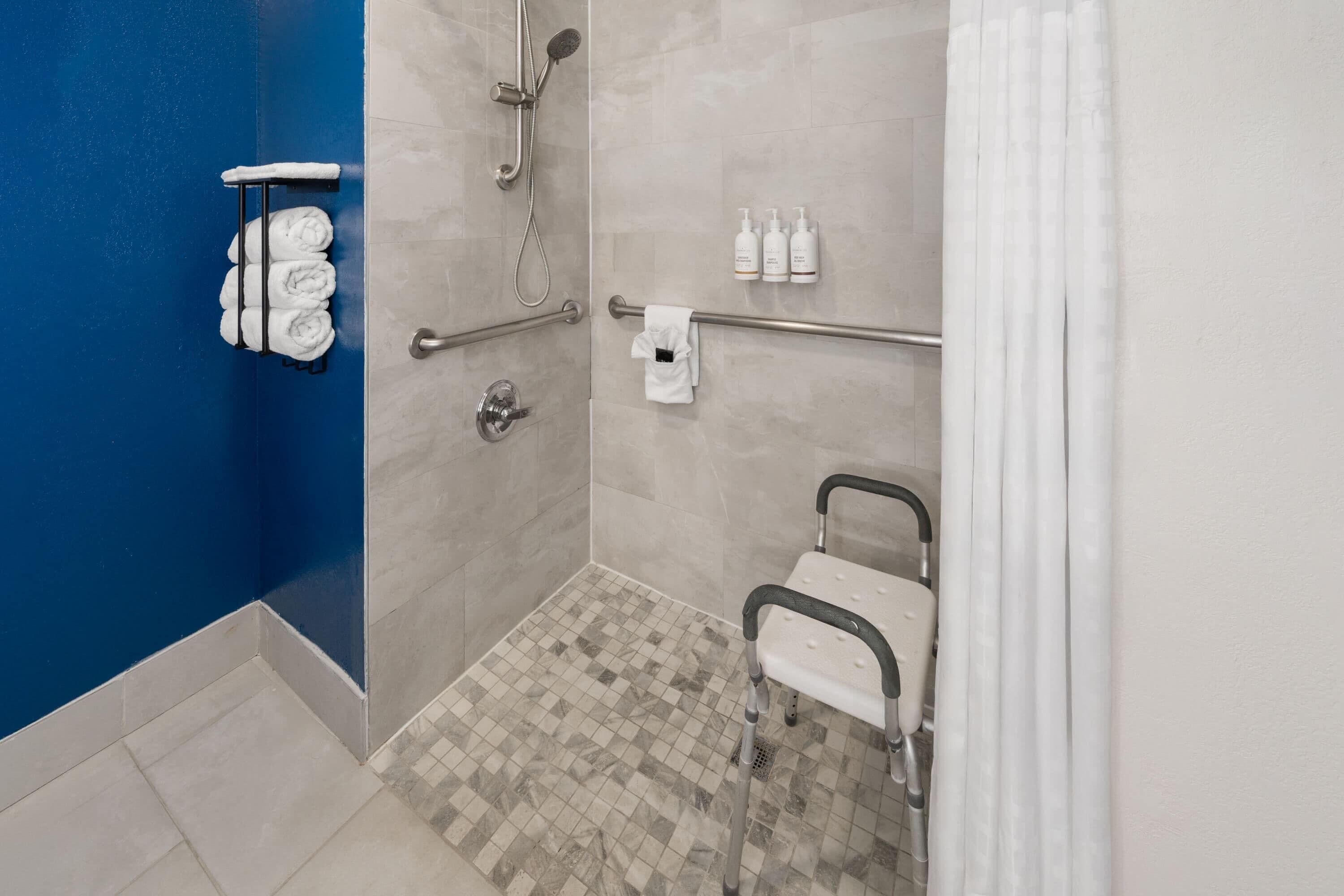 A bathroom with a shower, grab bars, a wheelchair-accessible bench, and a towel rack.