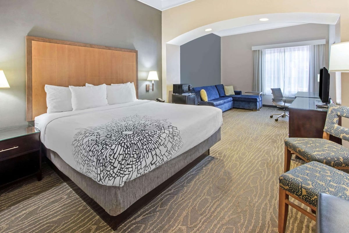 Quarto de hotel com uma cama grande, um sofá, uma escrivaninha e uma televisão.