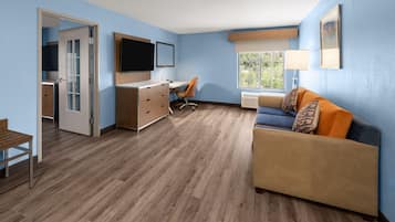 A compact living space with a kitchenette, a sofa, a desk, and a television.