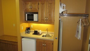 A compact kitchen with wooden cabinets, a microwave, a coffee maker, and a refrigerator.