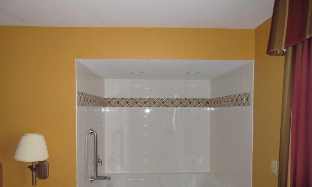 A bathroom with a shower, a handrail, and a wall-mounted lamp.