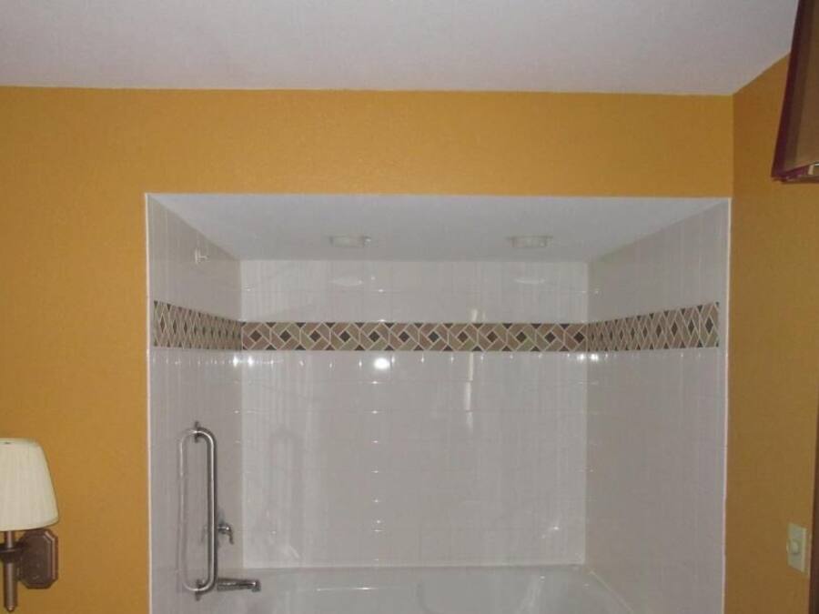 A bathroom with a shower, a handrail, and a wall-mounted lamp.
