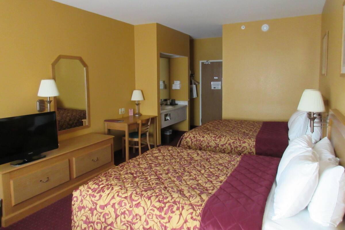 Habitación de hotel con dos camas, un escritorio, televisor y espejo.