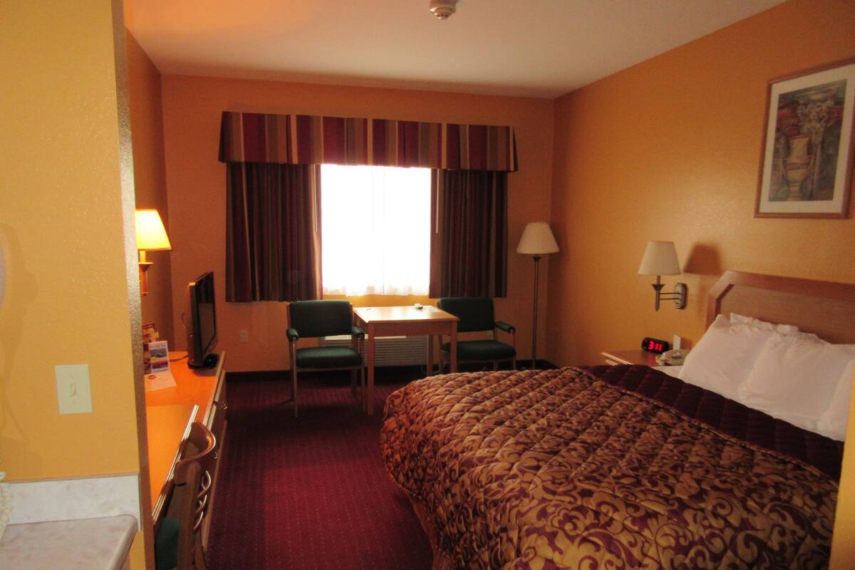 Una habitación de hotel con cama, escritorio, silla, mesa y ventana con cortinas.