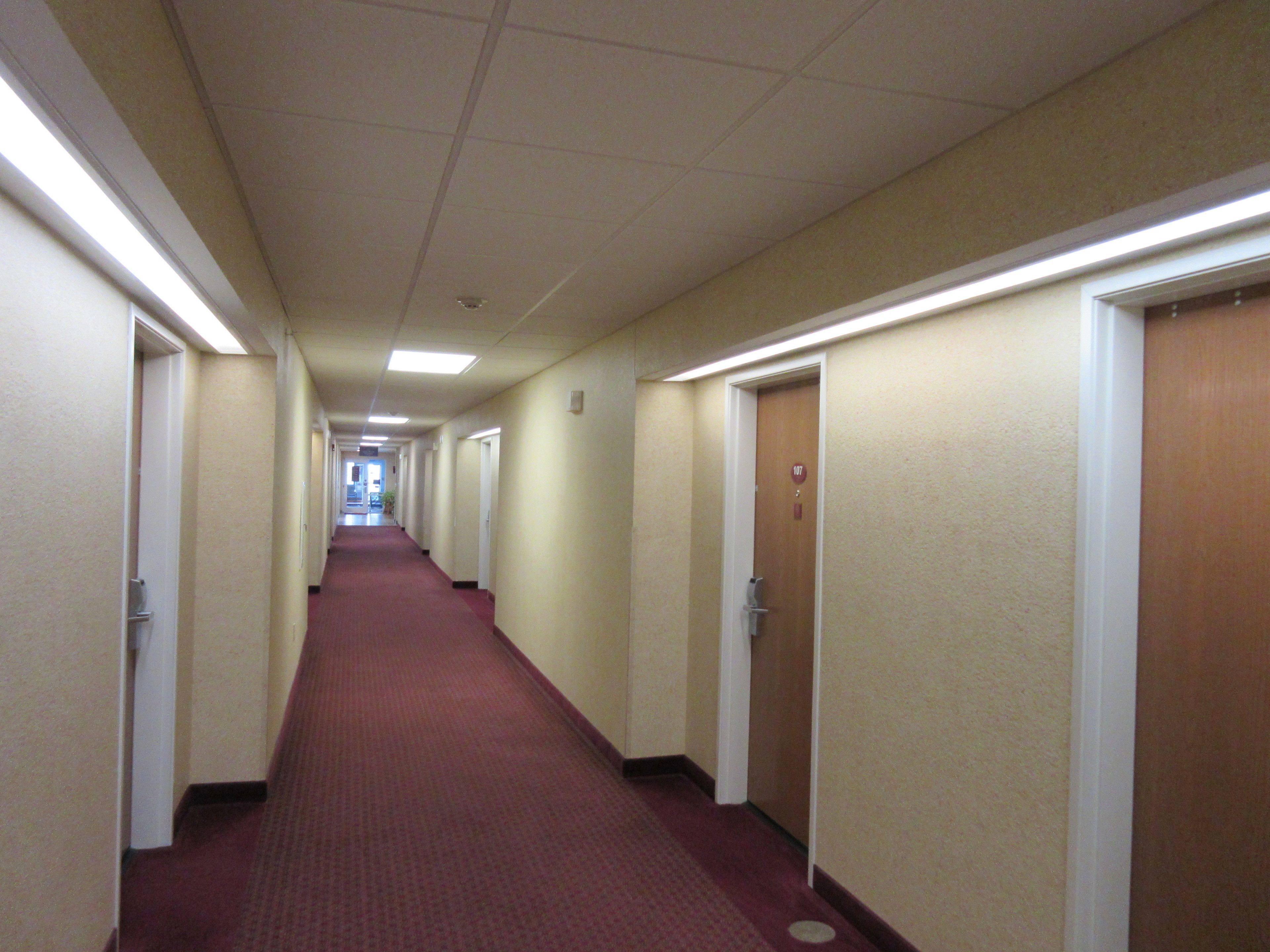 A long, narrow hotel corridor with carpeted floors and doors on both sides.