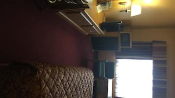 Una habitación de hotel con cama, escritorio, silla, televisor y ventana con cortinas.