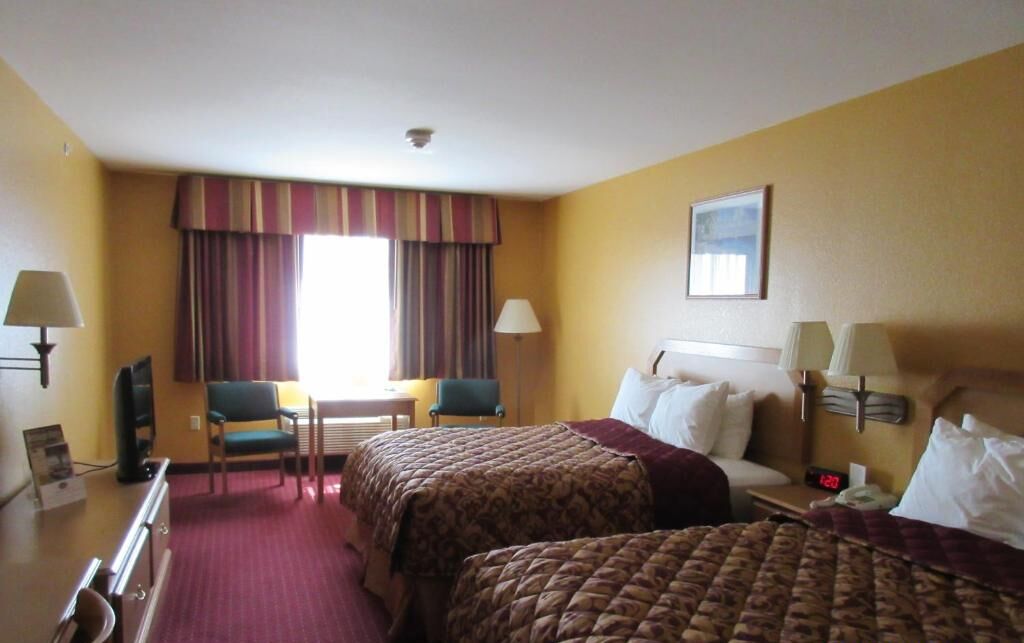 Une chambre d’hôtel avec deux lits, un bureau, une chaise et un téléviseur.
