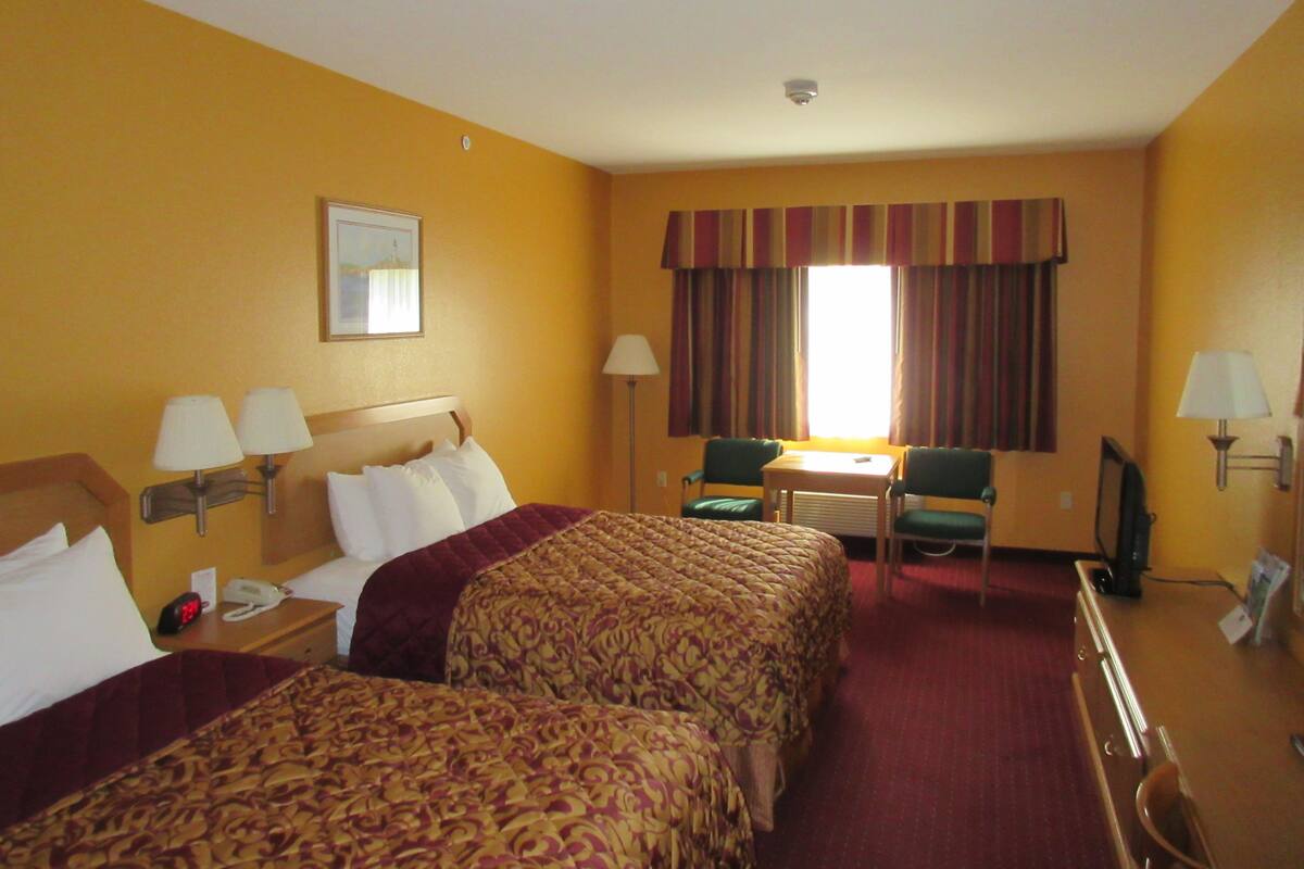Habitación de hotel con dos camas, un escritorio, dos sillas, un televisor y una ventana con cortinas.