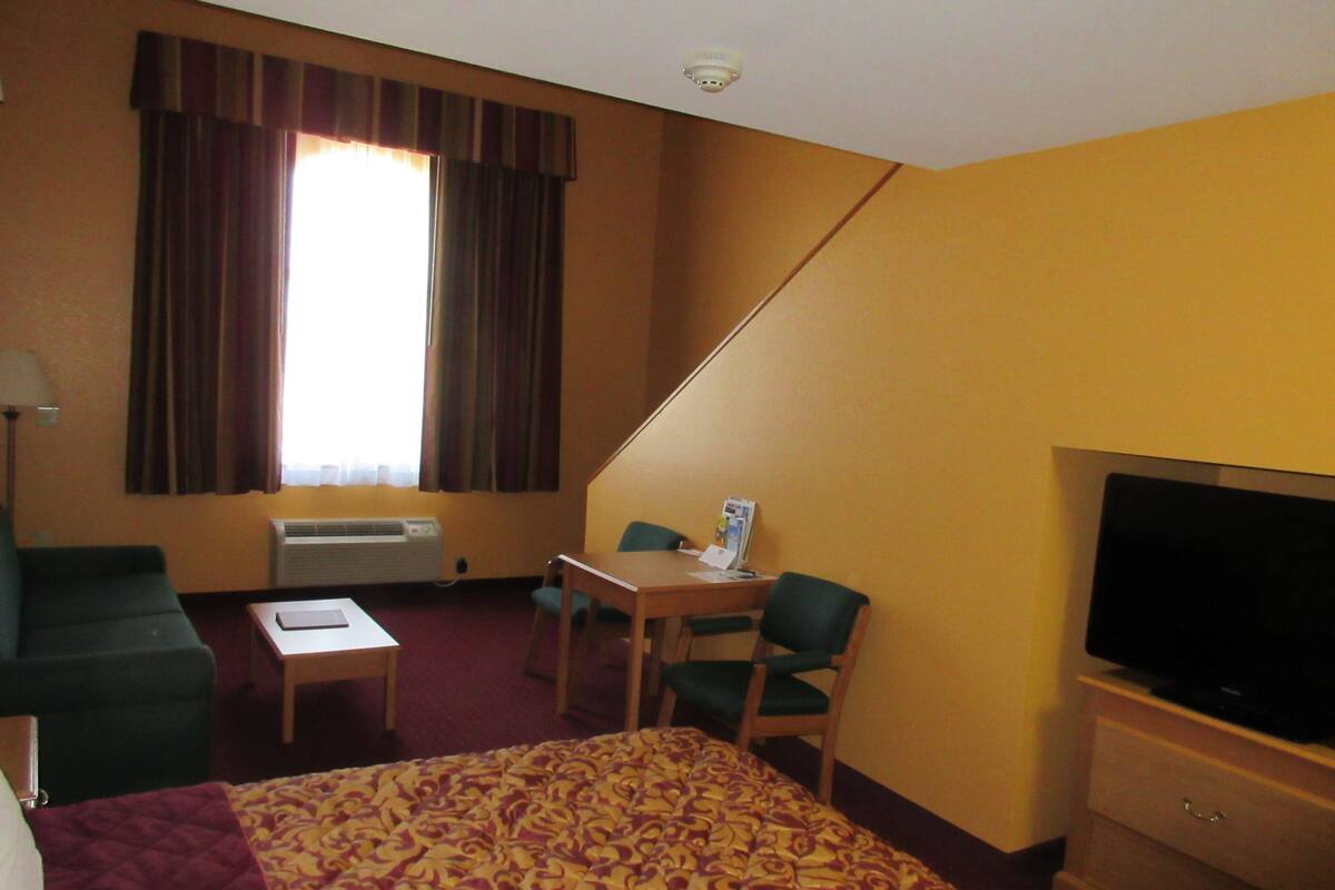 Habitación de hotel con cama, escritorio, silla, televisor y ventana con cortinas.
