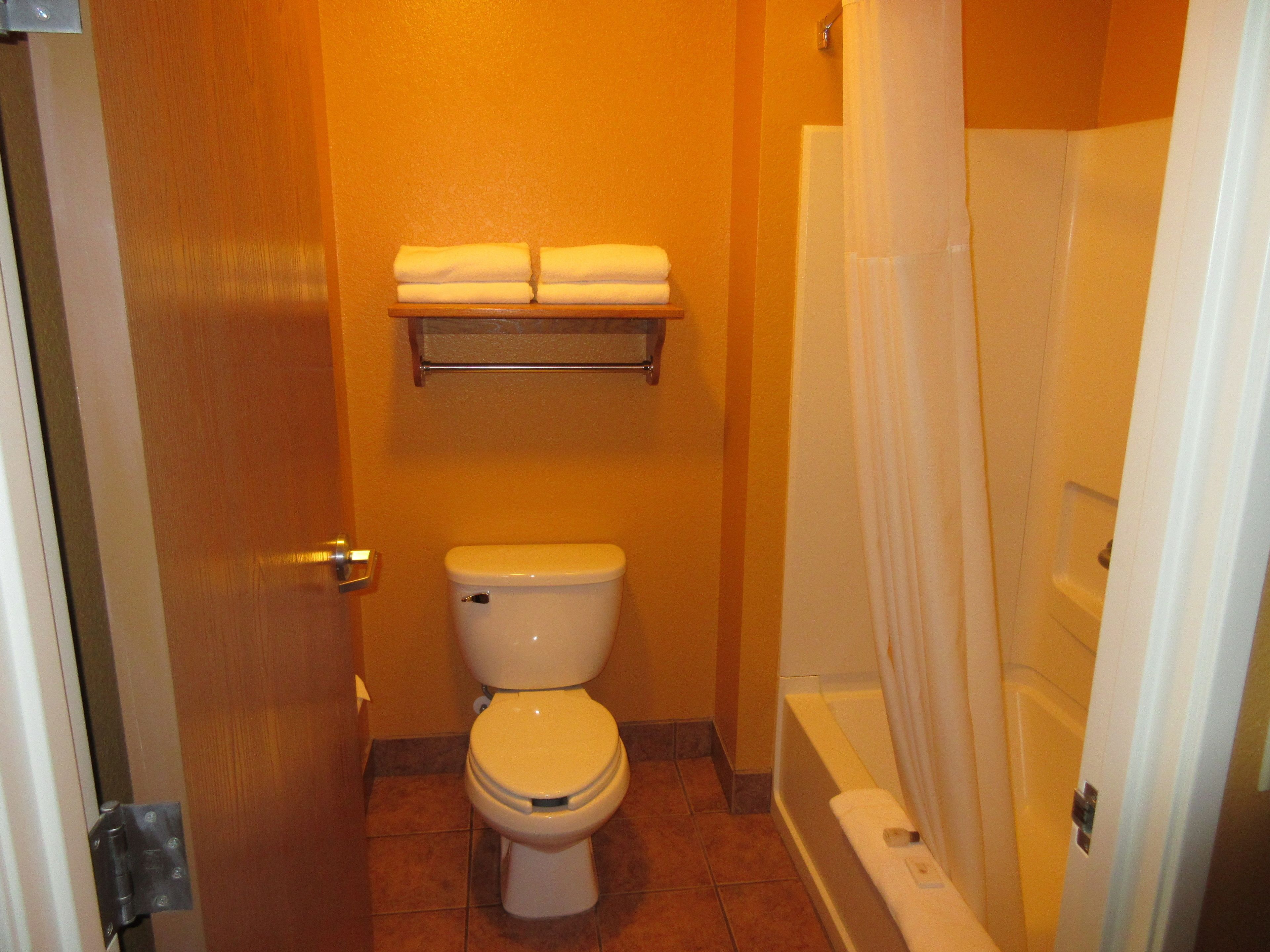 A bathroom with a toilet, a shelf with towels, and a bathtub.