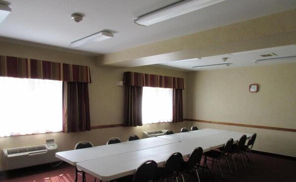 Une salle de conférence équipée d’une longue table, de chaises, de climatiseurs et de fenêtres avec des rideaux.