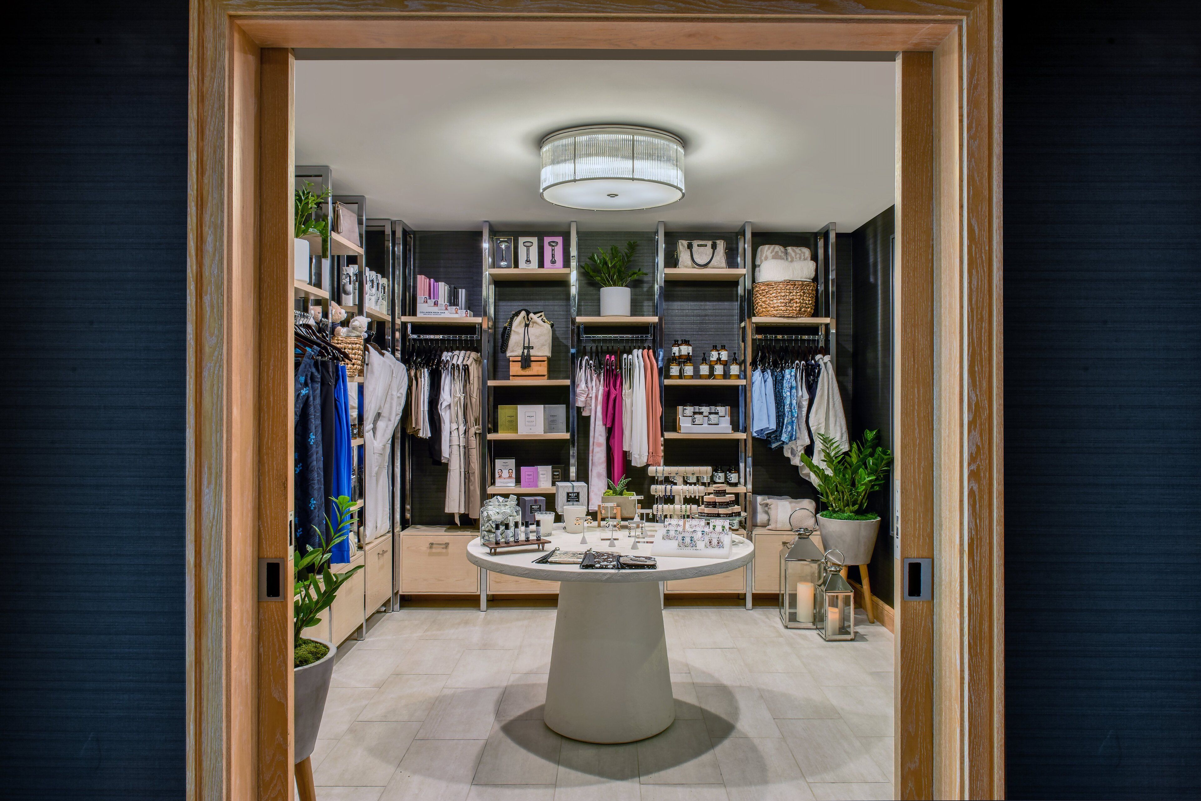 A well-organized boutique hotel room with a central round table, shelves with neatly arranged clothing and accessories, and a variety of decorative items.