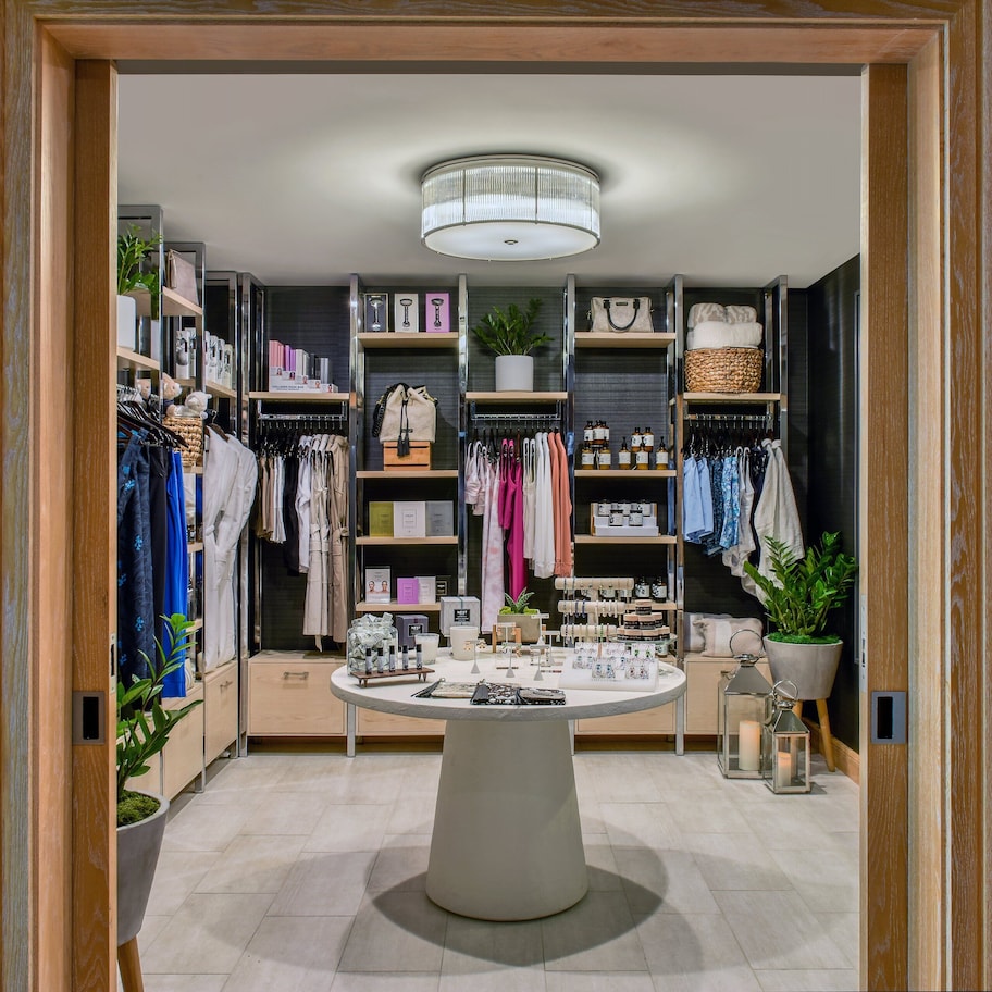 A well-organized boutique hotel room with a central round table, shelves with neatly arranged clothing and accessories, and a variety of decorative items.
