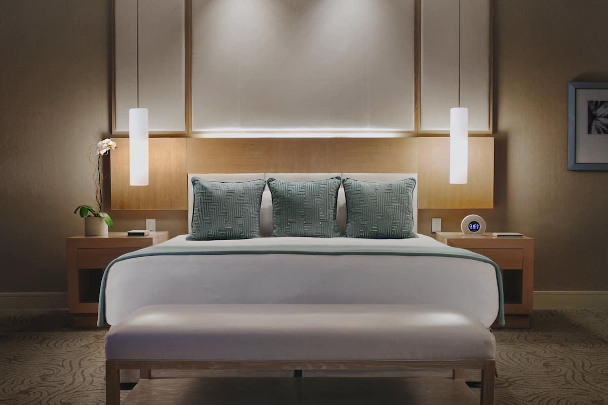 A neatly arranged bedroom with a bed, two bedside tables, a nightstand, a wall-mounted clock, and a framed picture.
