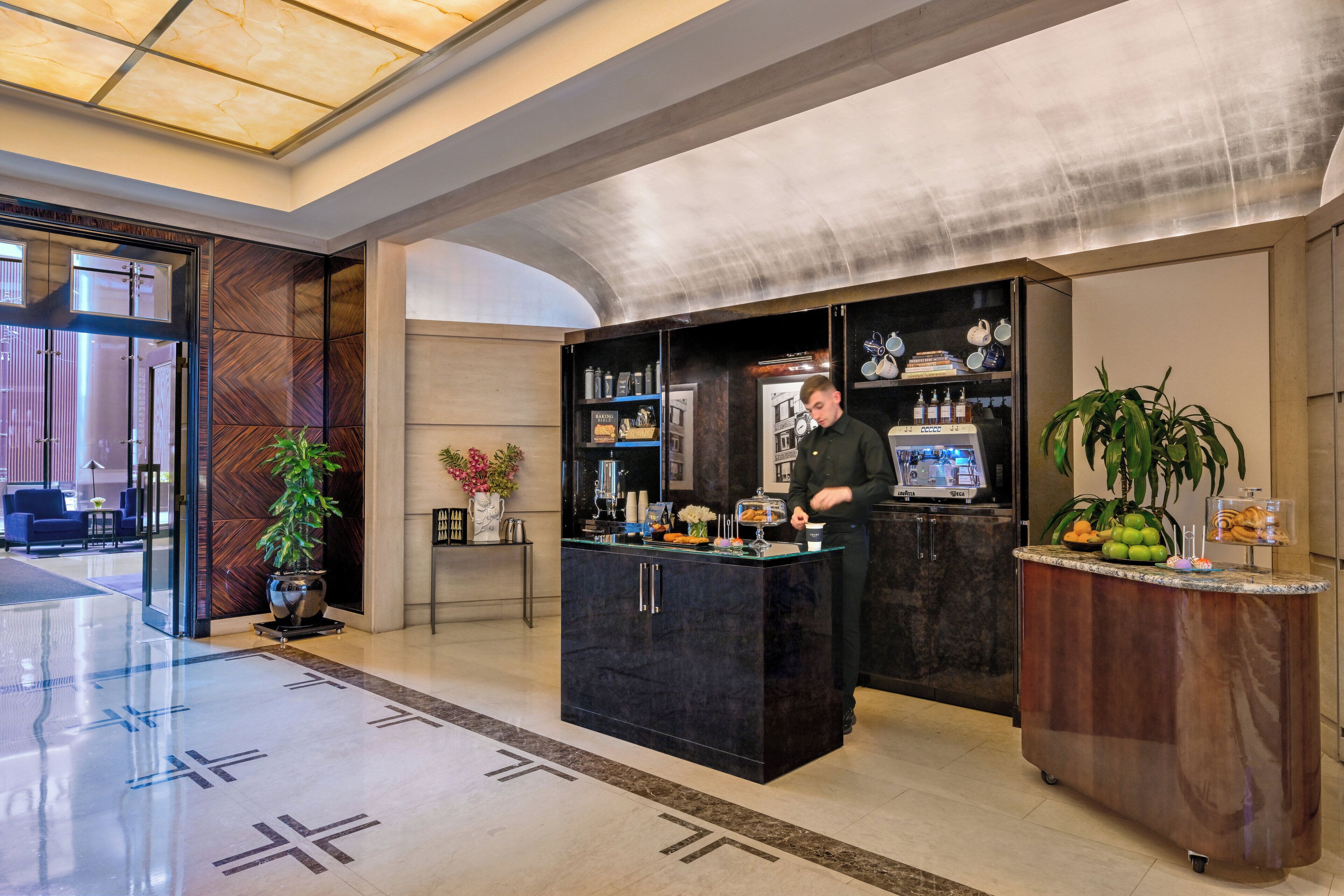 A hotel lobby with a reception desk, a coffee station, and a seating area with chairs and a potted plant.