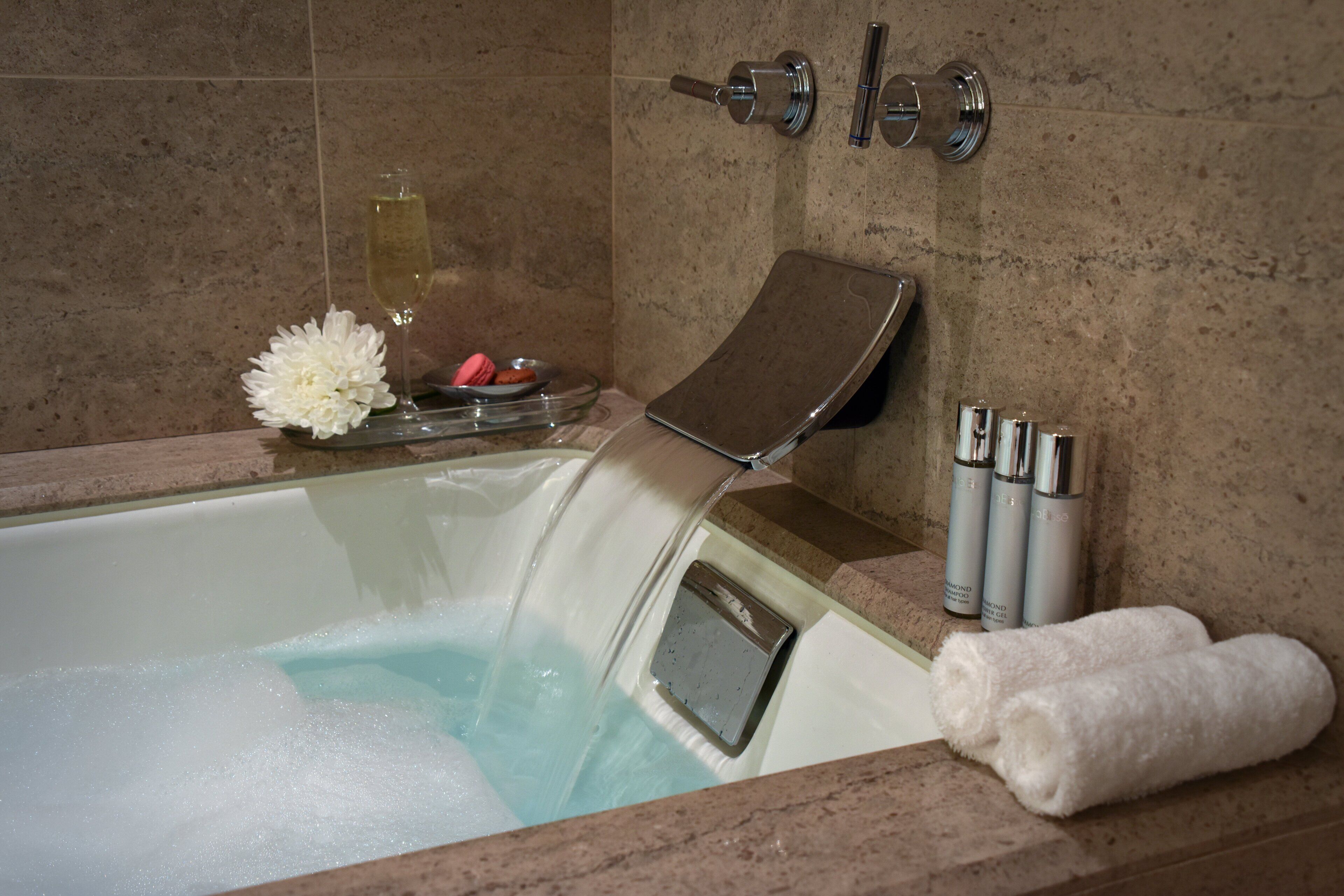 A bathtub with a glass panel, a flower arrangement, and a bottle of shampoo.