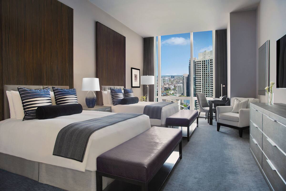A modern hotel room with a large bed, a desk, a chair, and a view of the city.