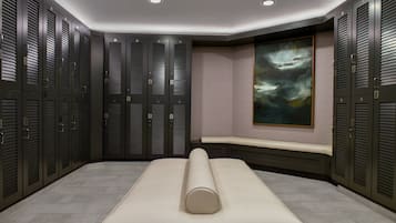A modern locker room with multiple lockers, a bench, and a large abstract painting on the wall.