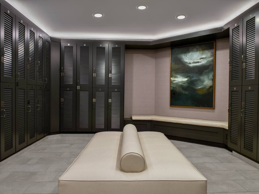 A modern locker room with multiple lockers, a bench, and a large abstract painting on the wall.