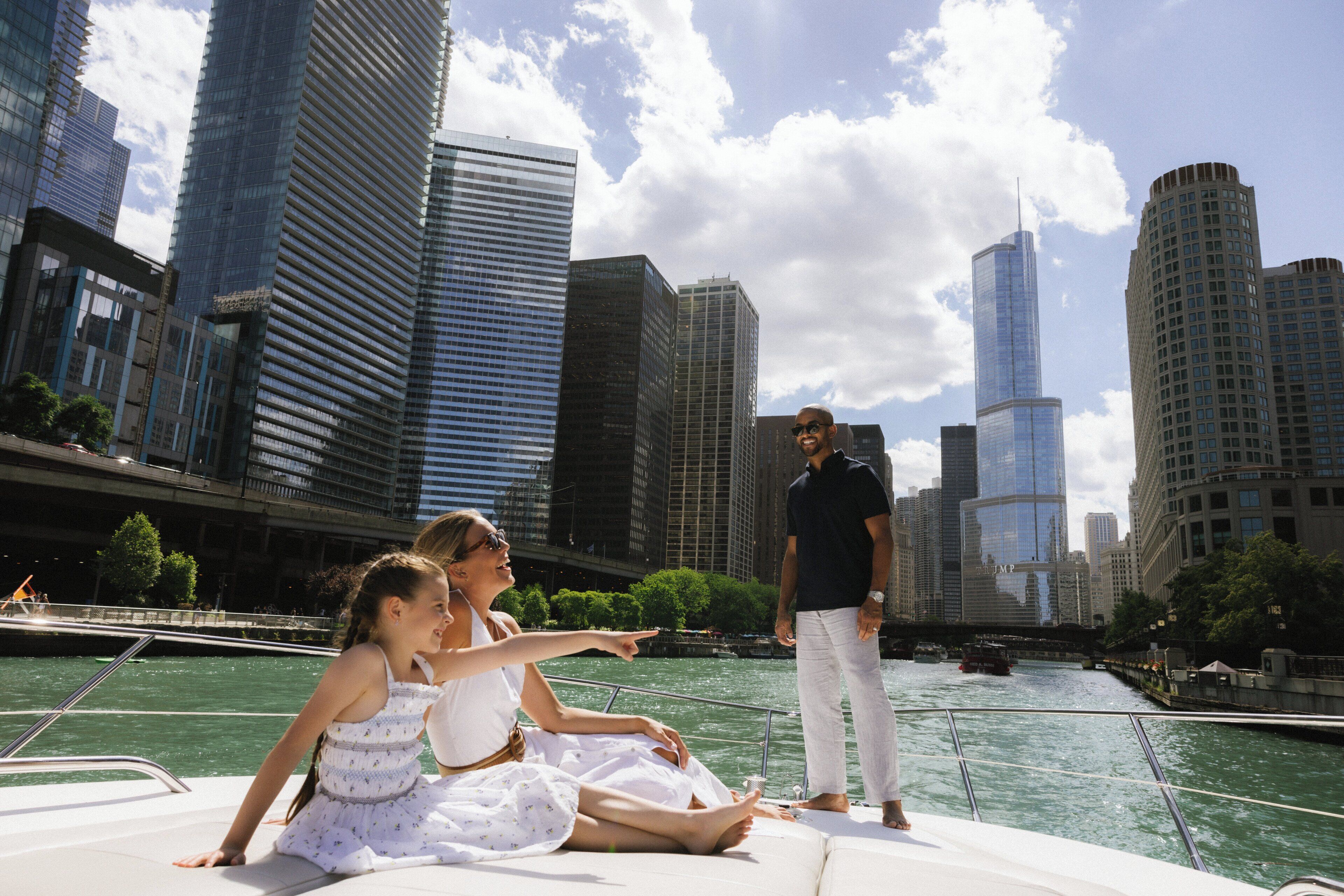 A boat with people on it, a river, and tall buildings in the background.