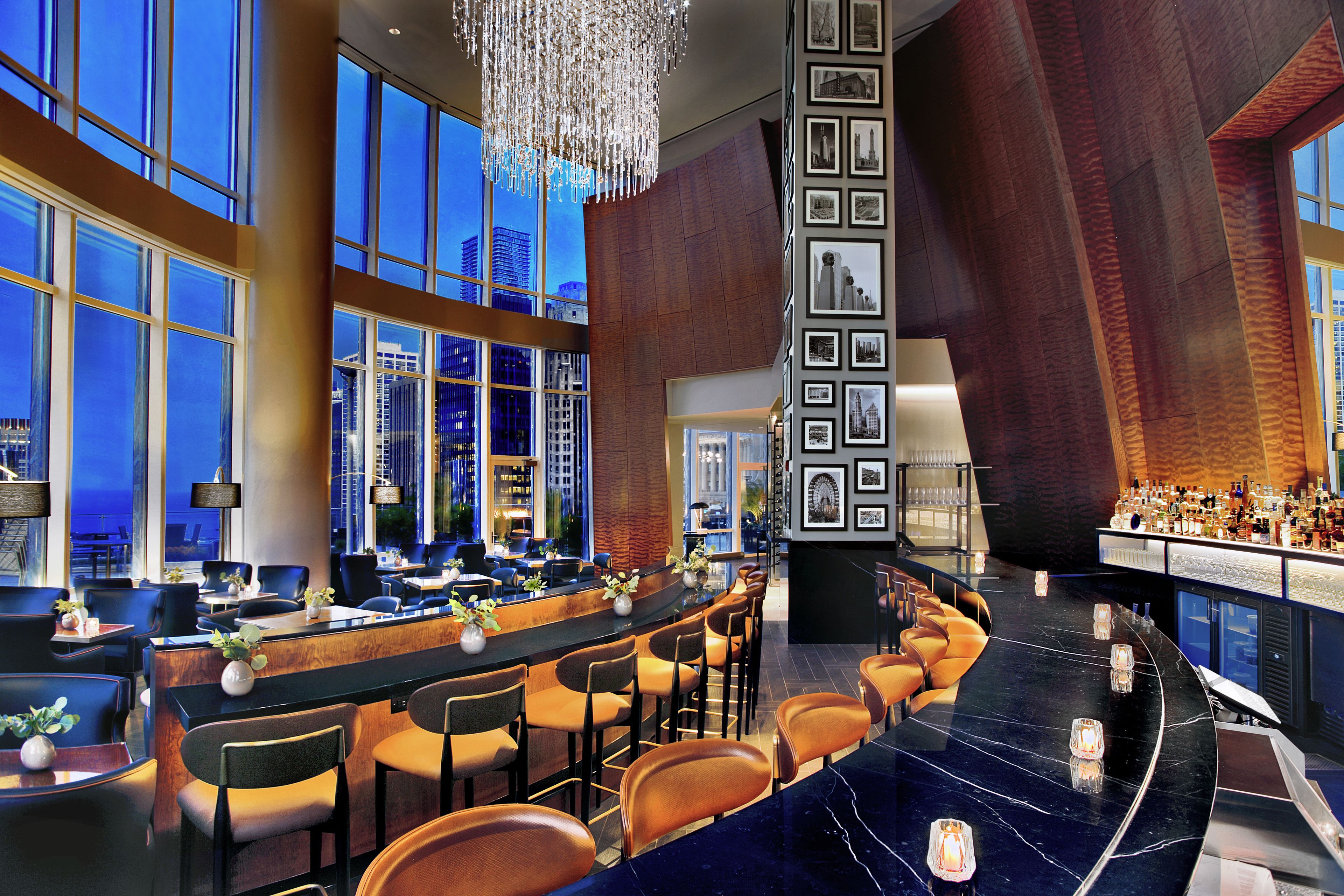A modern bar area with a curved marble countertop, bar stools, and a city view through large windows.