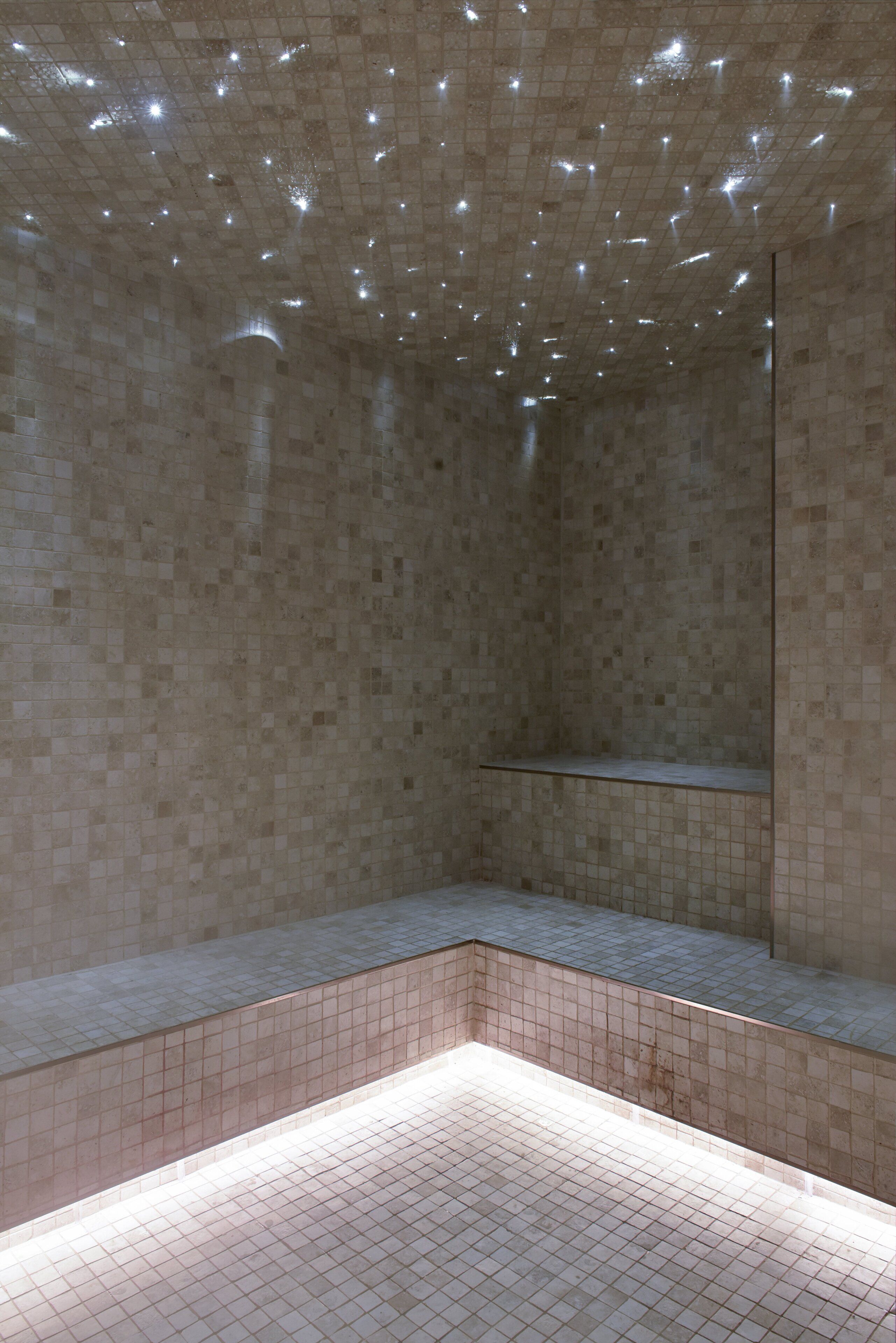 A tiled shower area with a rectangular bench and a wall-mounted mirror.