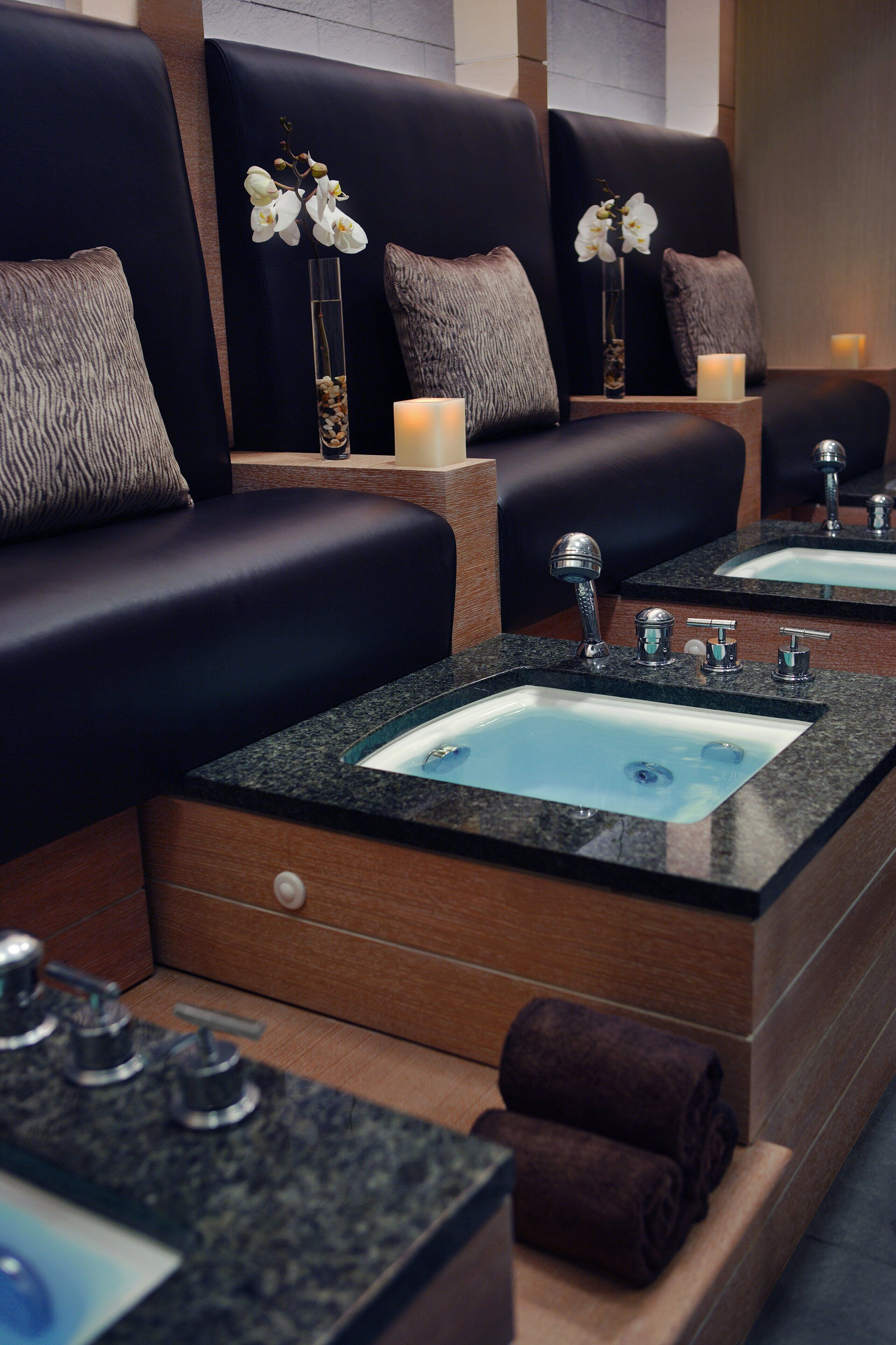 Un espace spa moderne avec des sièges en cuir noir, des vasques en marbre et des vases décoratifs ornés de fleurs blanches.