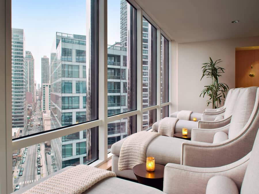 Una habitación de hotel moderna con un ventanal que ofrece vistas a la ciudad, una zona de estar acogedora con una planta y una pequeña mesa con una vela.