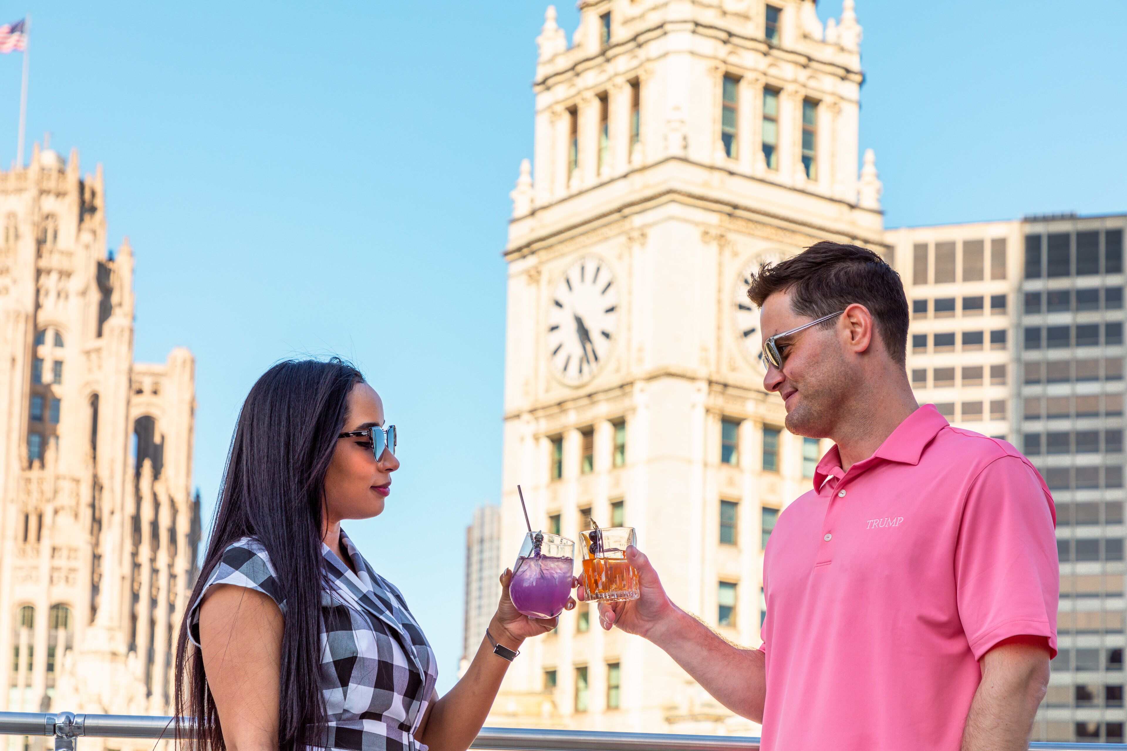 A couple holding drinks in front of a historic building with a clock tower.