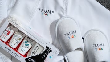 Un par de zapatillas blancas con el bordado "TRUMP kids", junto con una camisa blanca y una caja de productos para bebés.