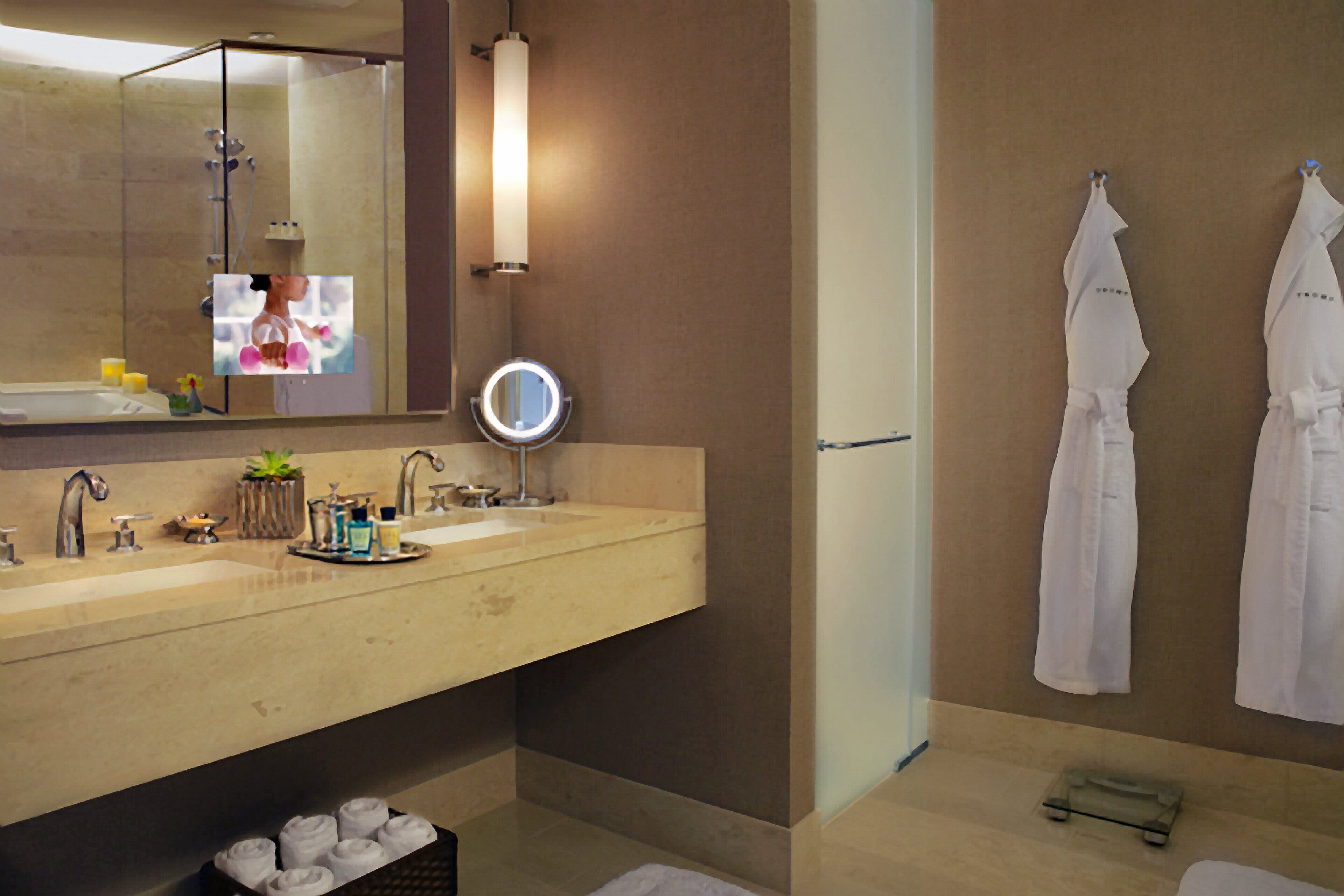 A modern bathroom with a large mirror, two sinks, a round mirror, and two white robes hanging on the wall.